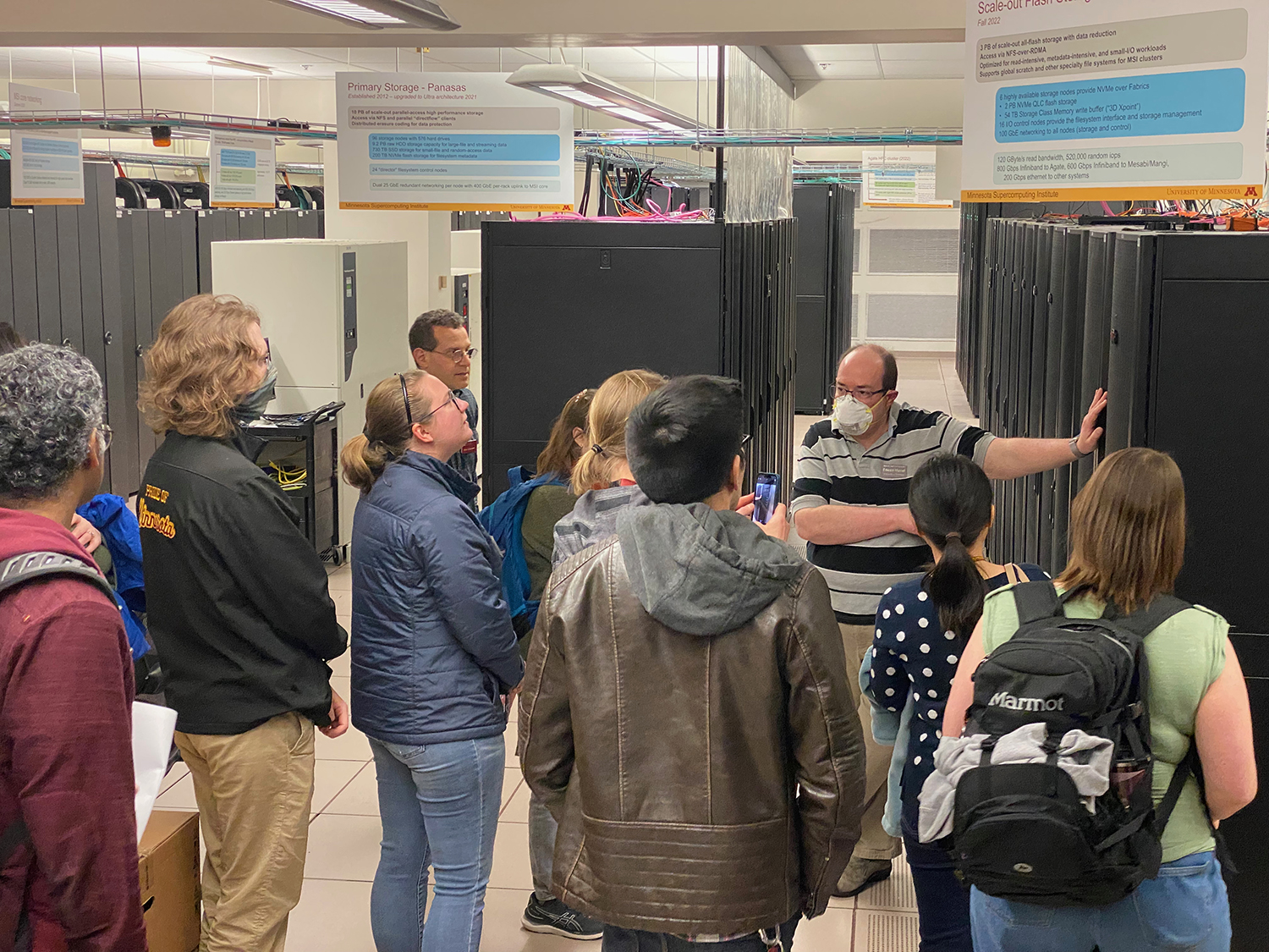 man leading a tour group gestures towards supercomputers 