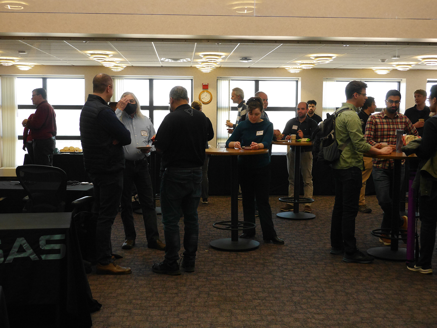 group of people stand at tables, having refreshments