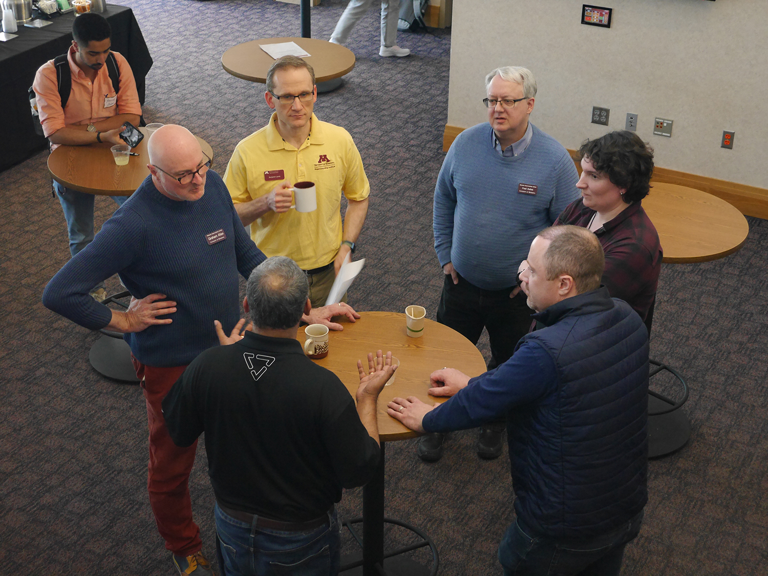 group of people talking and standing around a small round table